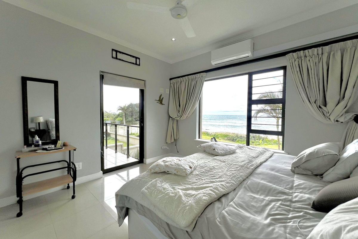 A bright bedroom featuring tiled floors, a ceiling fan, air conditioning, and direct access to a balcony with scenic ocean views.