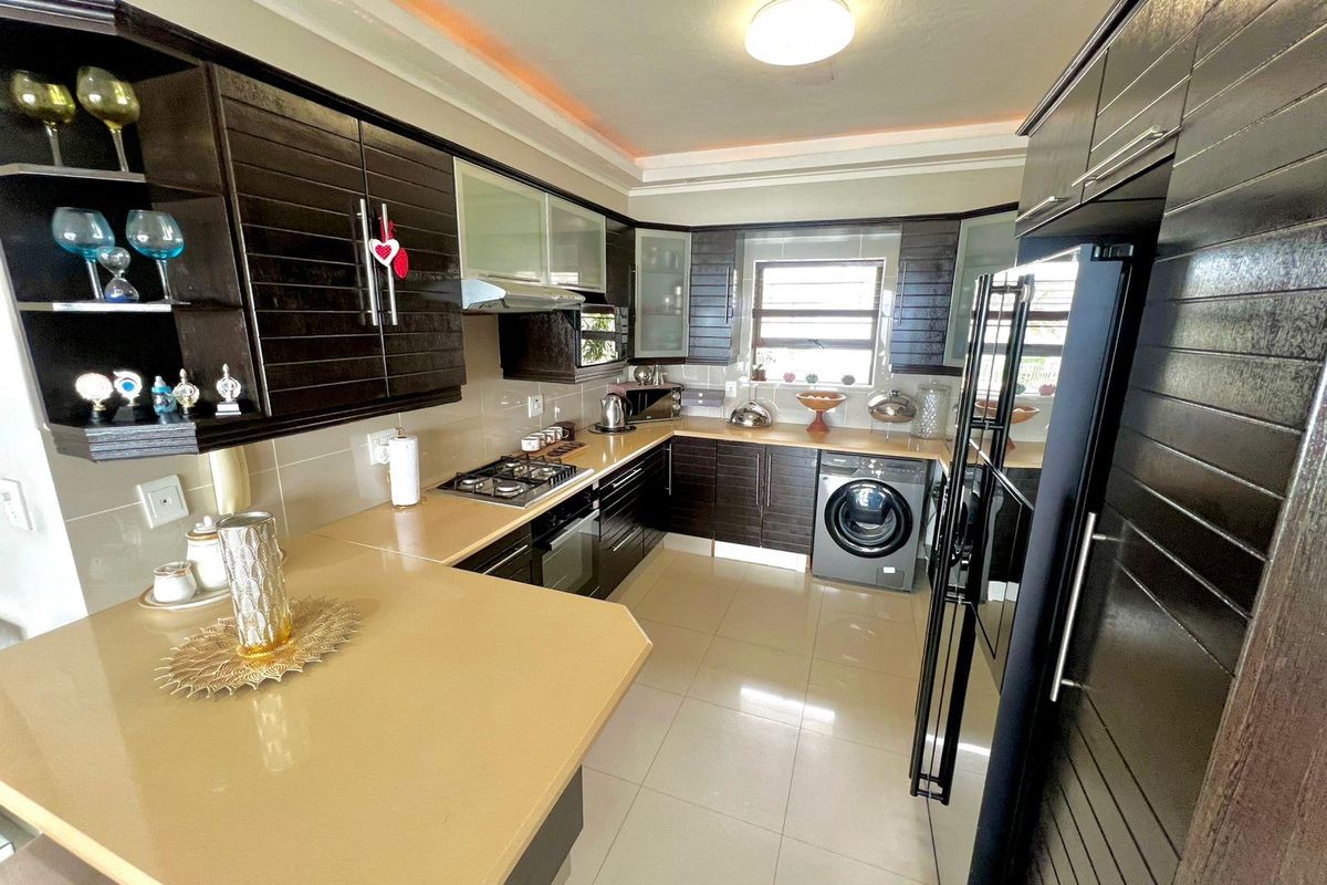 Modern kitchen featuring dark wood cabinetry, stone countertops, built-in gas hob, oven, extractor fan, and integrated laundry appliance with tiled flooring.