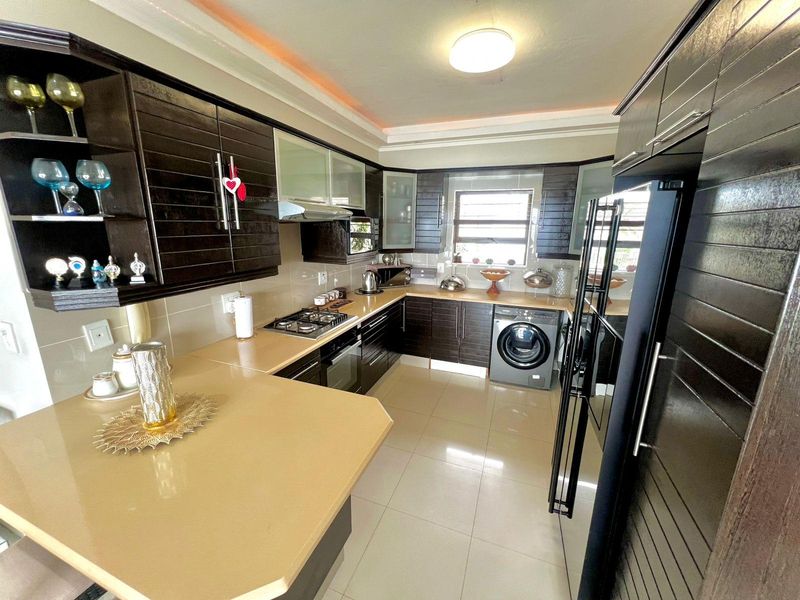 Modern kitchen featuring dark wood cabinetry, stone countertops, built-in gas hob, oven, extractor fan, and integrated laundry appliance with tiled flooring.