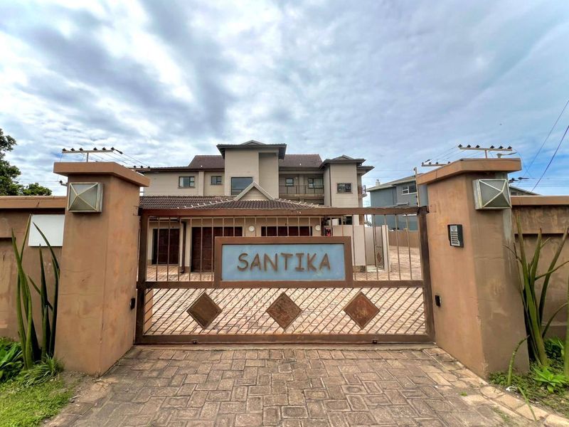Front elevation of the Santika apartment complex featuring a secure gated entrance, paved driveway, and perimeter wall with integrated security fencing.
