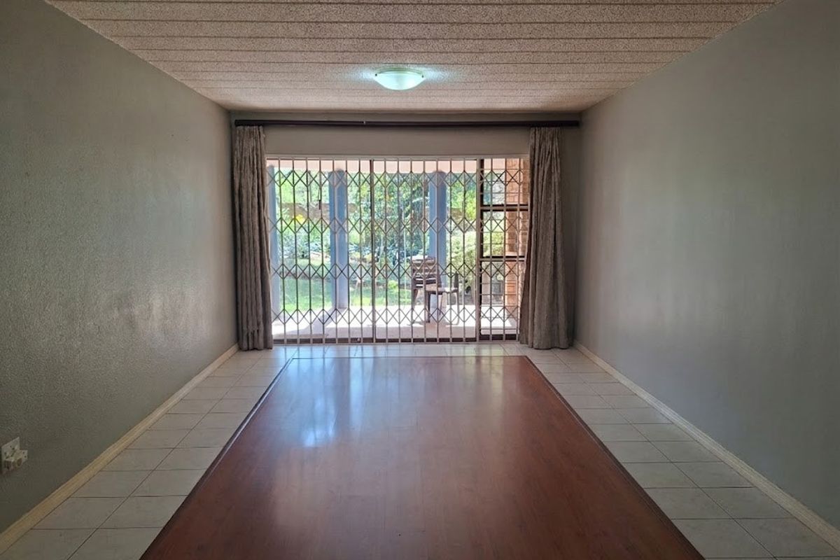 An empty living room featuring laminate flooring with a tiled border, textured ceiling, and a sliding door leading to an outdoor area with security gates.