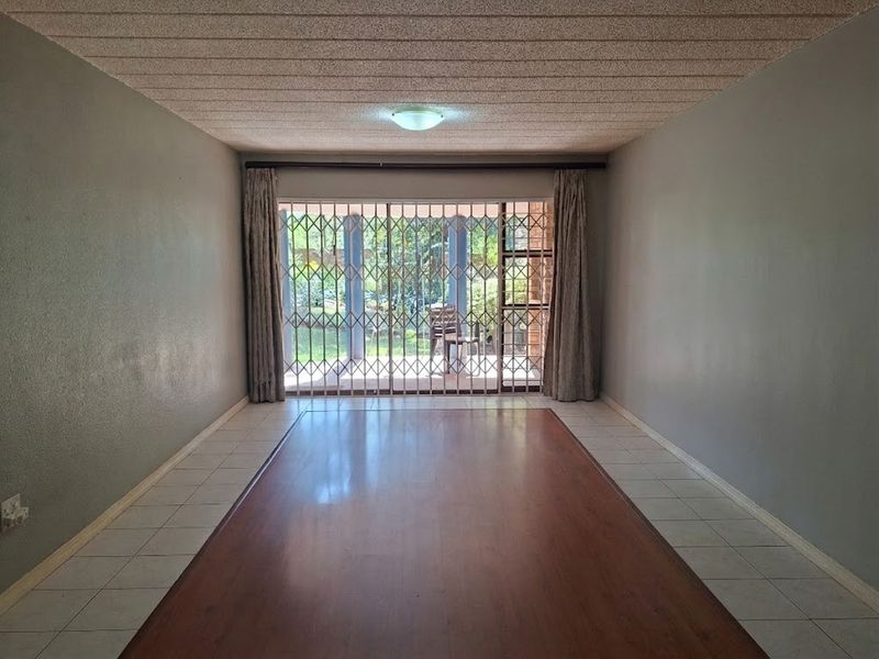 An empty living room featuring laminate flooring with a tiled border, textured ceiling, and a sliding door leading to an outdoor area with security gates.