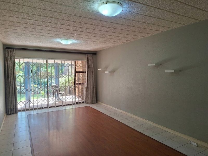 Spacious living area featuring a mix of laminate and tiled flooring, textured ceiling, and a sliding glass door with security gate leading to the patio.