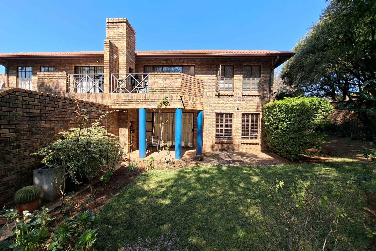 Rear view of a double-story brick apartment building featuring a private garden, ground-floor patio, and an upper-level balcony with metal railings.