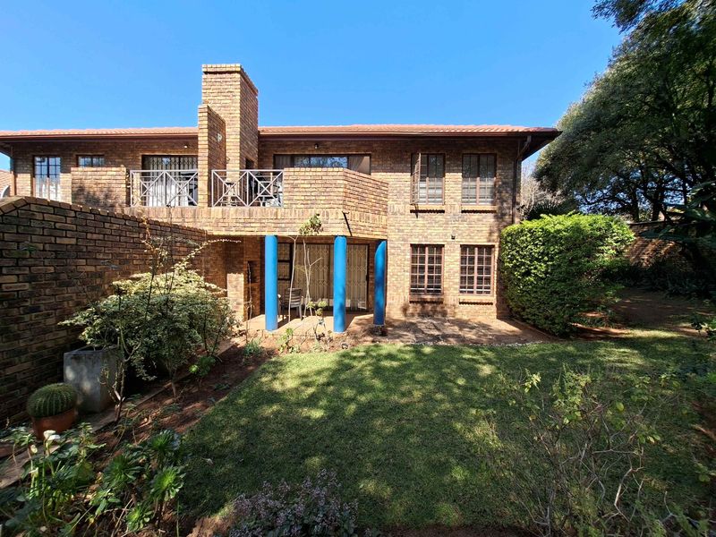 Rear view of a double-story brick apartment building featuring a private garden, ground-floor patio, and an upper-level balcony with metal railings.