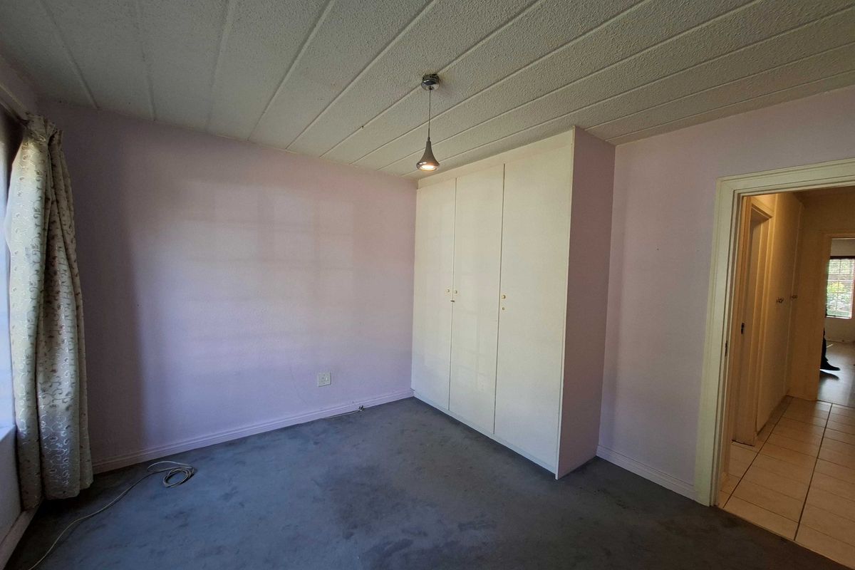 A vacant bedroom featuring built-in wardrobes, carpeted flooring, and a simple pendant light fixture, offering a blank canvas for potential updates.