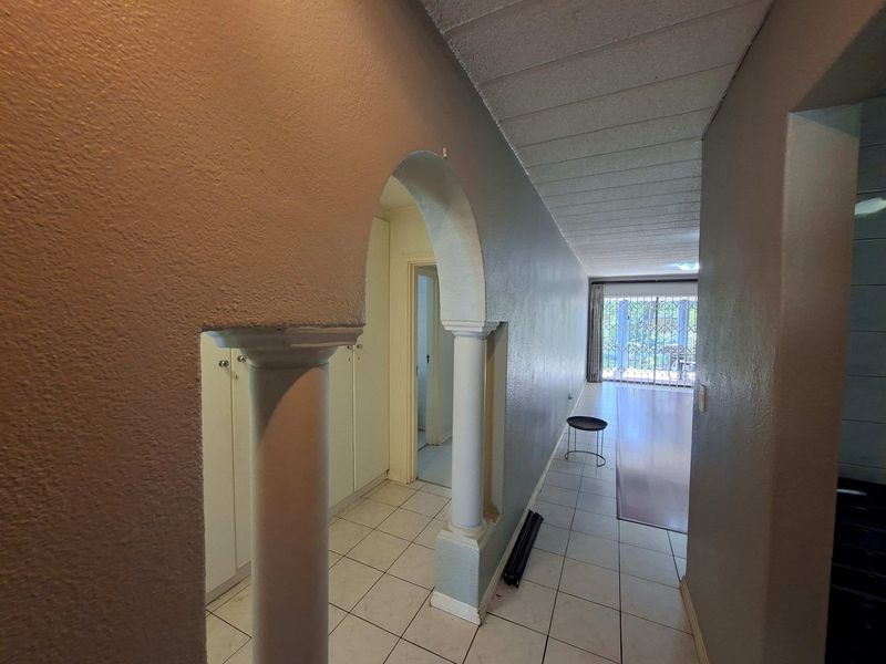 A tiled hallway featuring an arched architectural detail, built-in storage cupboards, and access to the living area with a security gate.
