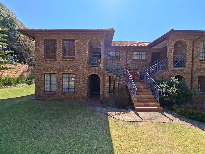 Exterior view of a two-story face brick apartment building featuring an external staircase, paved walkways, and established garden surroundings.