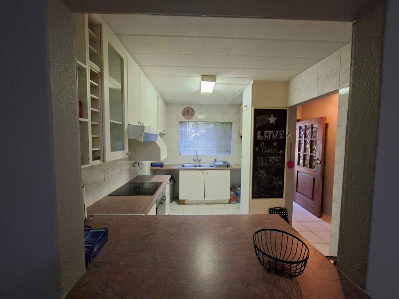 A functional kitchen featuring built-in cabinetry, laminate countertops, an electric hob, and tiled finishes, offering potential for modernization.