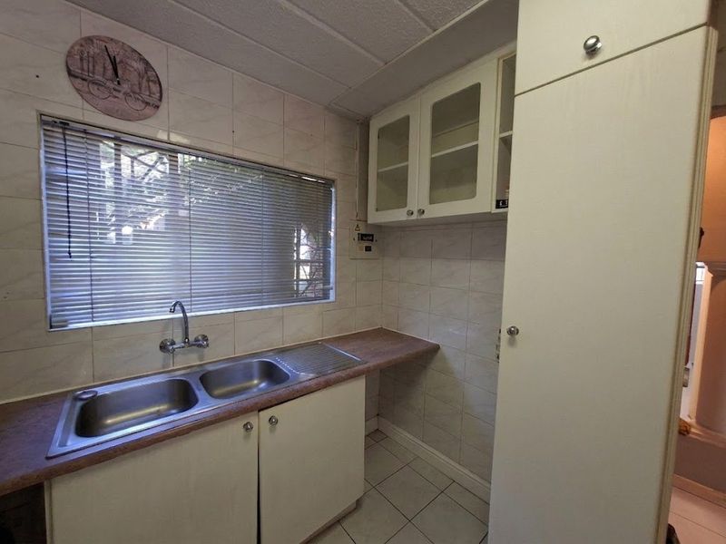 A functional kitchen area featuring built-in cabinetry, a double stainless steel sink, tiled backsplash, and tiled flooring.