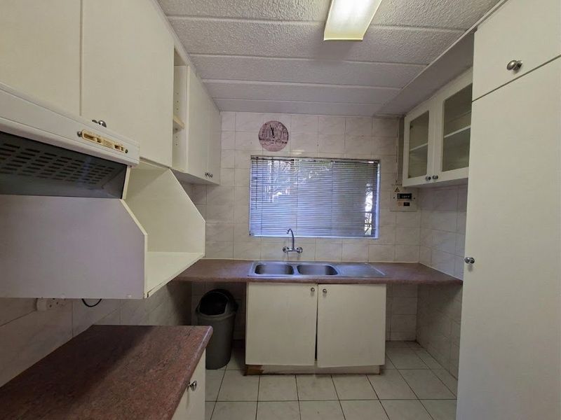 A functional kitchen featuring built-in cabinetry, laminate countertops, a double bowl sink, and tiled finishes, offering potential for modernization.