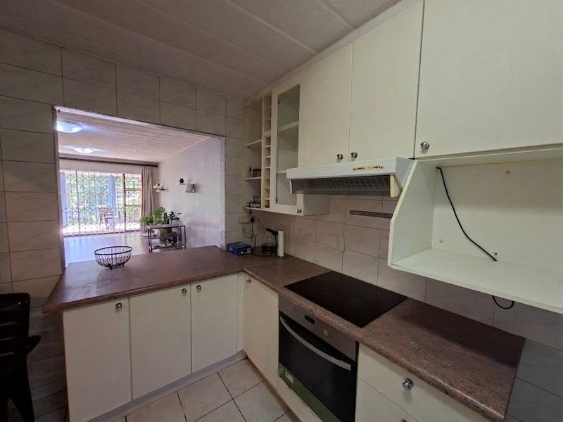 A functional kitchen featuring built-in cabinetry, laminate countertops, an integrated oven, and an electric hob, with an open-plan layout connecting to the living area.