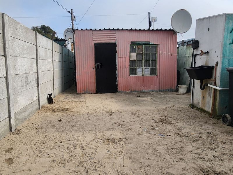Rear exterior view of a corrugated iron structure featuring a precast concrete boundary wall and an external utility sink area.