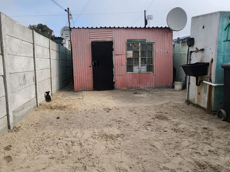 Rear view of a residential structure featuring corrugated metal siding, a precast concrete boundary wall, and an external utility sink area.
