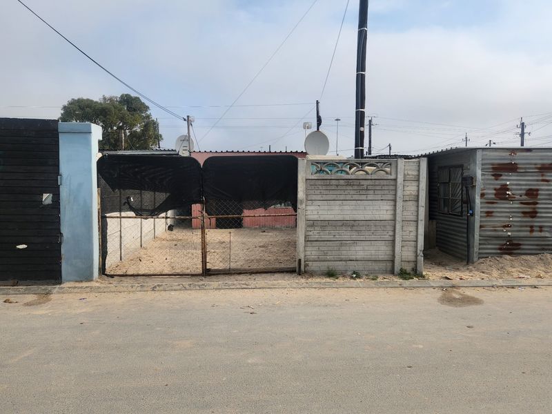 Front view of a residential plot featuring a metal gate, precast concrete boundary wall, and a corrugated metal structure.