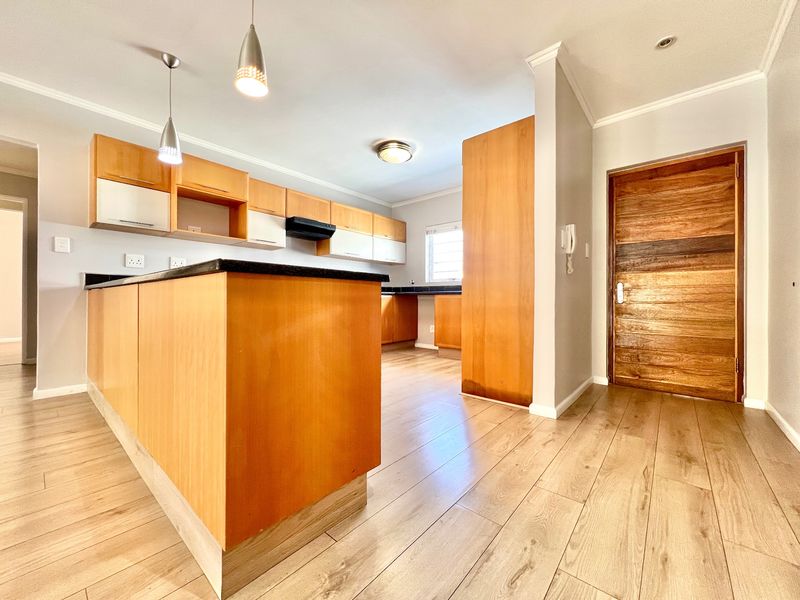 A bright, open-plan kitchen featuring light wood cabinetry, contrasting black granite countertops, laminate flooring, and modern pendant lighting.