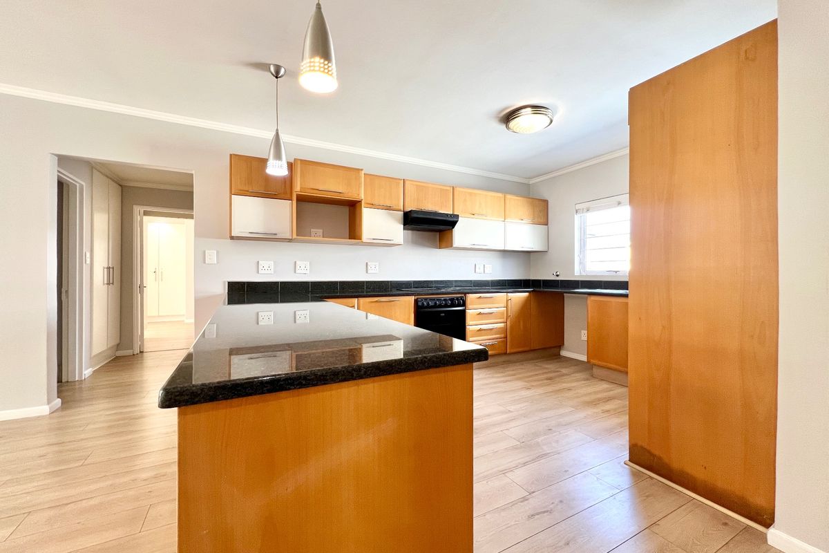 Spacious kitchen featuring granite countertops, ample wooden cabinetry, built-in stove with extractor fan, and modern laminate flooring in an open-plan layout.