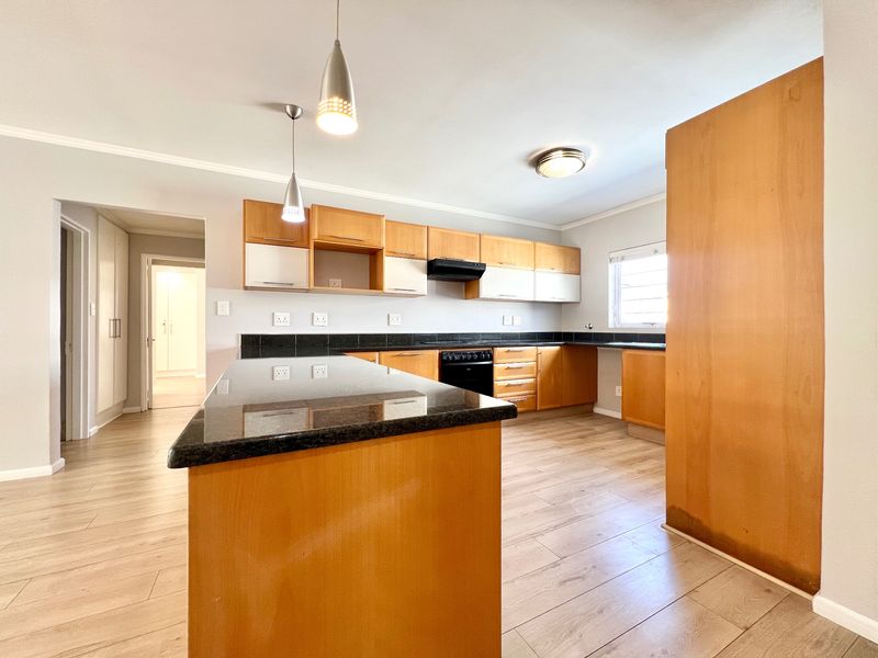 Spacious kitchen featuring granite countertops, ample wooden cabinetry, built-in stove with extractor fan, and modern laminate flooring in an open-plan layout.