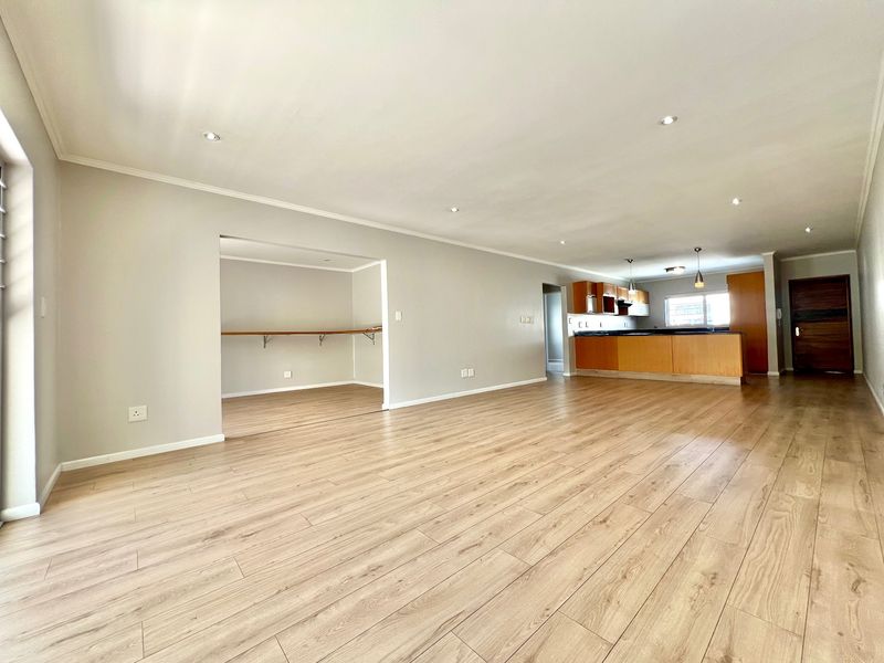 Spacious open-plan living area featuring light laminate flooring, recessed lighting, and a functional kitchen with a breakfast bar and ample cabinetry.