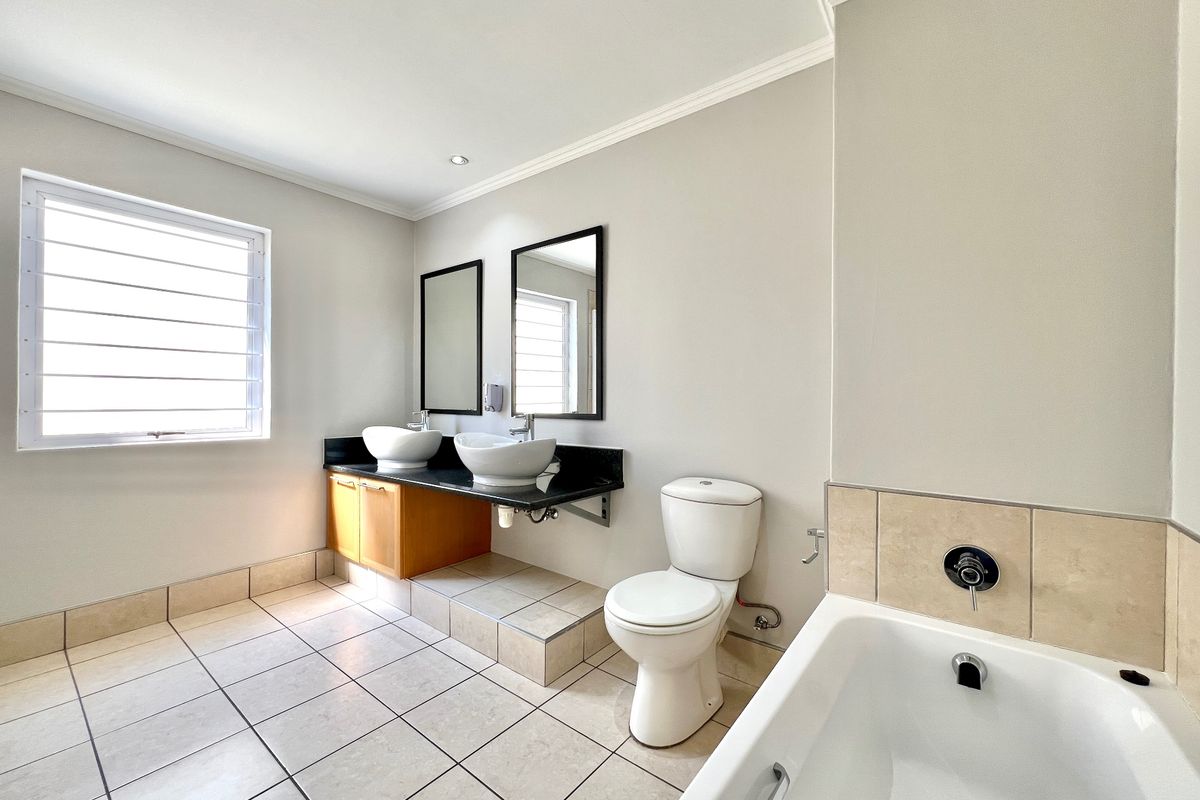 A spacious, well-lit bathroom featuring a double vanity with vessel sinks, granite countertops, a bathtub, and neutral tiled flooring.