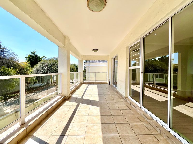 A spacious, covered balcony featuring tiled flooring, a modern glass balustrade, and large sliding glass doors providing access to the interior.
