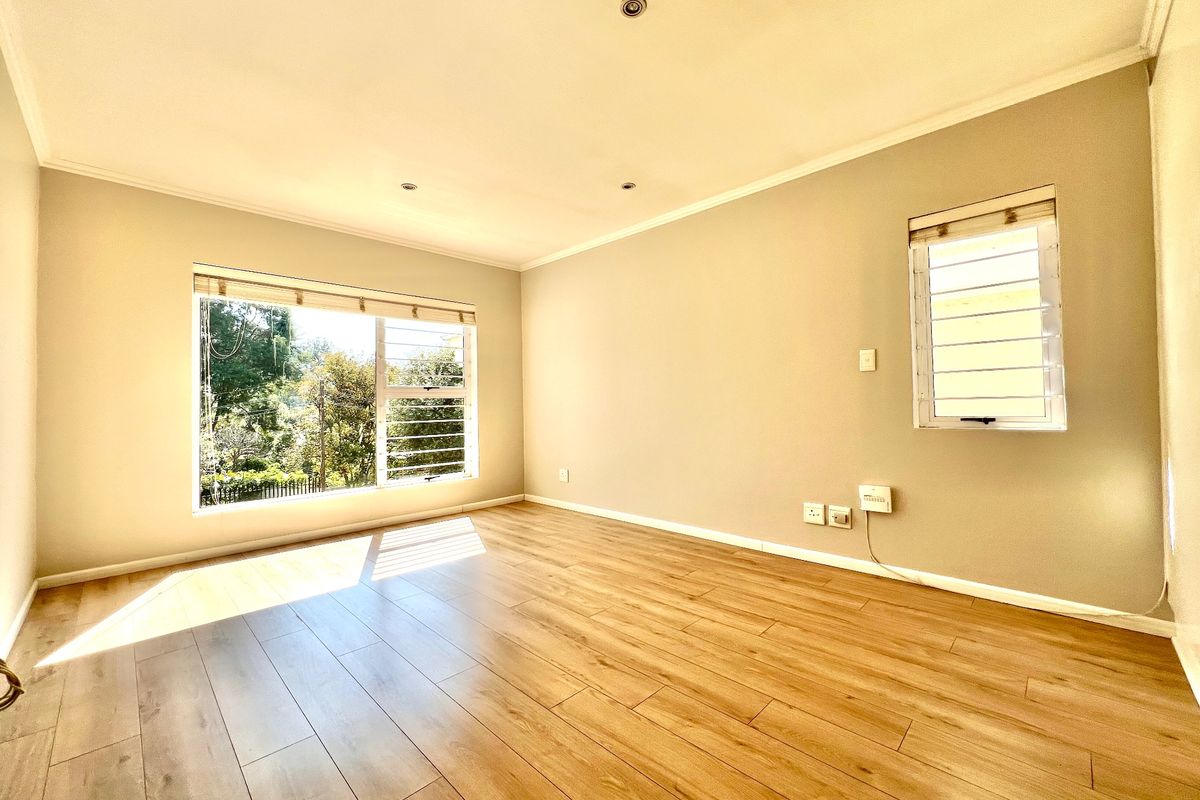 A bright, empty bedroom featuring modern laminate flooring, louvered windows, and recessed downlighting, offering a clean and neutral space ready for furnishing.