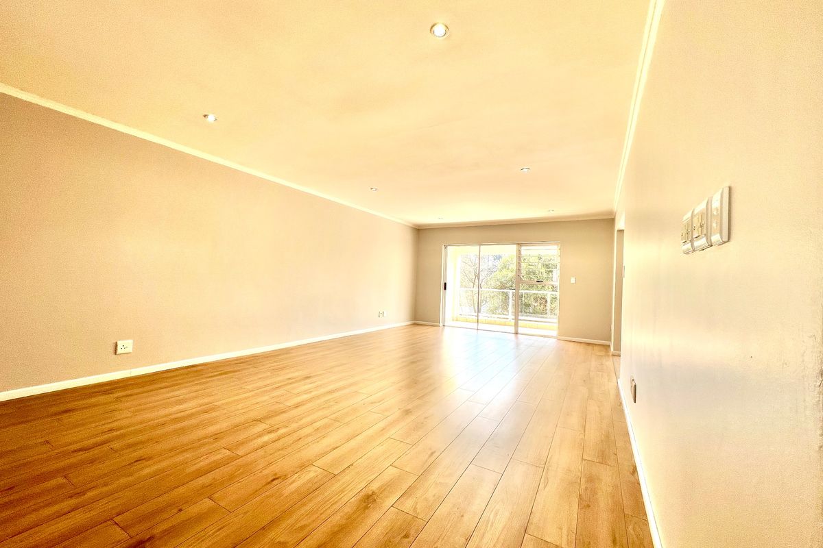 A spacious, empty living room featuring modern laminate flooring, recessed downlighting, and a large sliding glass door leading to an outdoor area.