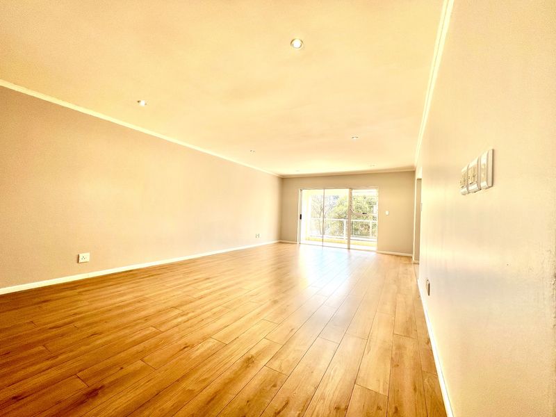 A spacious, empty living room featuring modern laminate flooring, recessed downlighting, and a large sliding glass door leading to an outdoor area.