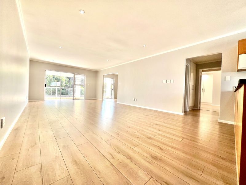 Spacious open-plan living area featuring light wood-look laminate flooring, recessed lighting, and large sliding glass doors leading to an outdoor balcony.