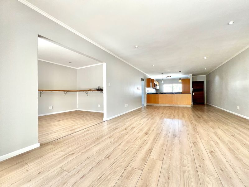 Spacious open-plan living area featuring light laminate flooring, recessed lighting, and a functional kitchen with wooden cabinetry and a breakfast bar.