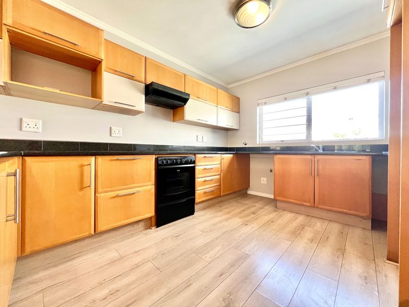 A functional kitchen featuring wooden cabinetry, black granite countertops, a built-in oven with extractor fan, and light-toned laminate flooring.