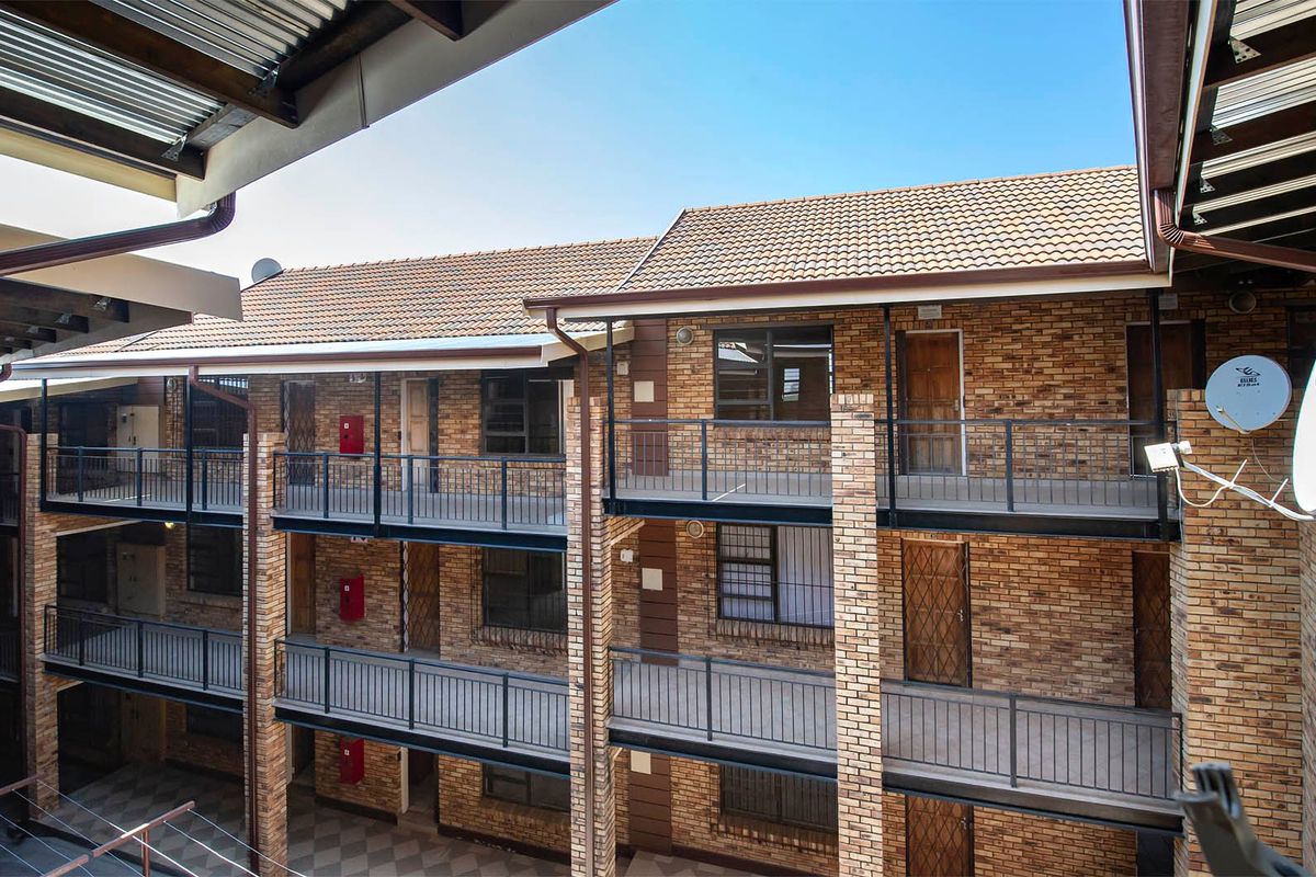 Exterior view of a multi-story apartment complex featuring face brick construction, tiled roofing, and open-air access balconies with metal railings.