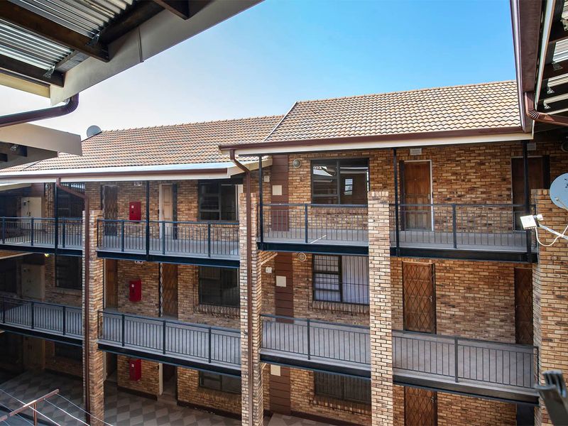 Exterior view of a multi-story apartment complex featuring face brick construction, tiled roofing, and open-air access balconies with metal railings.
