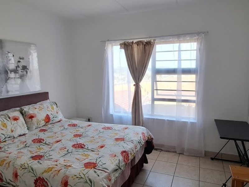 A functional bedroom featuring tiled flooring and a window fitted with security bars, providing natural light and ventilation.