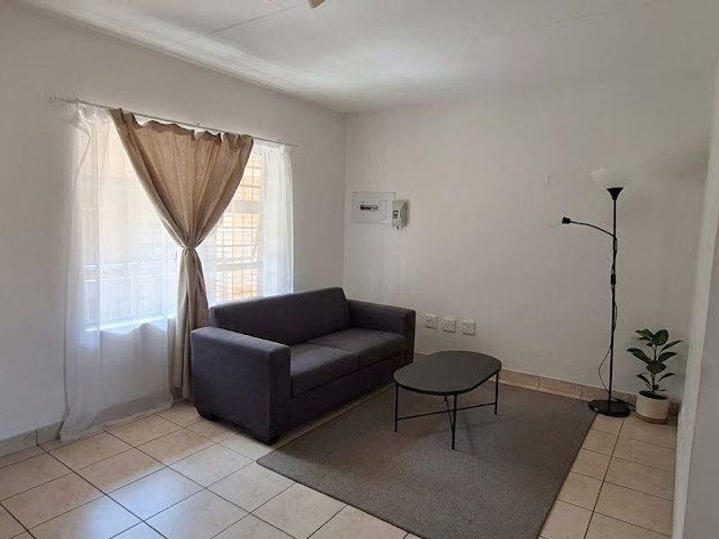 A simple living room featuring neutral tiled flooring and a wall-mounted electrical distribution board, offering a clean and functional space.