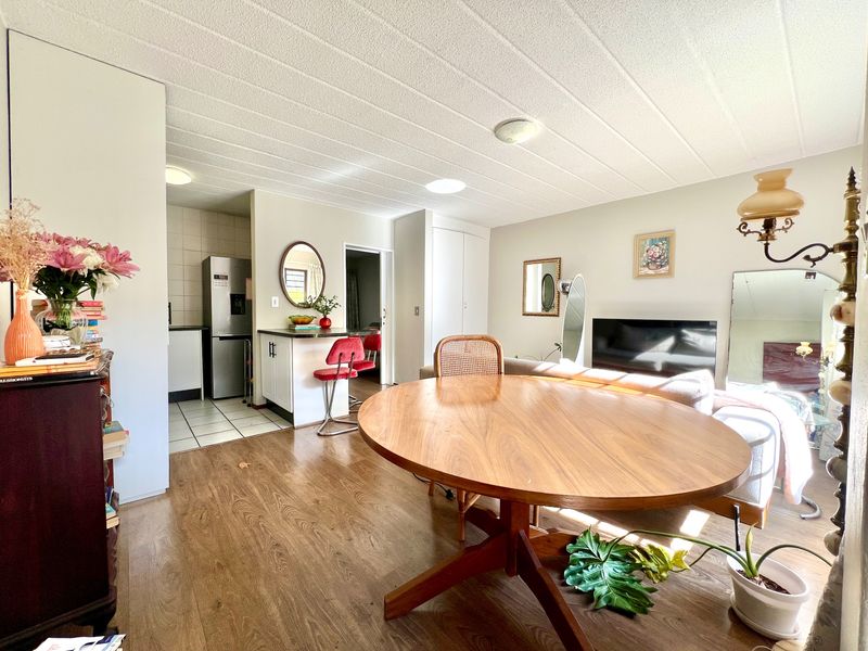 Open-plan living and dining area featuring laminate flooring, a breakfast bar, and an adjoining kitchen with tiled flooring and built-in cabinetry.