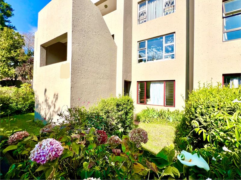 Rear view of a multi-story apartment building featuring textured exterior walls, aluminium windows with security bars, and a well-maintained garden area.