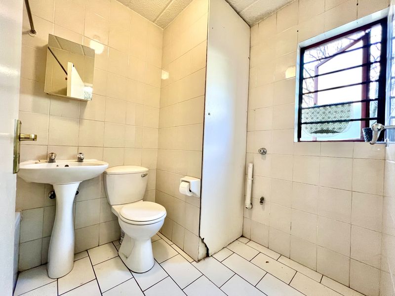 A dated bathroom featuring a pedestal basin, toilet, and fully tiled walls. The space is empty and requires cosmetic updates to modernize the finishes.