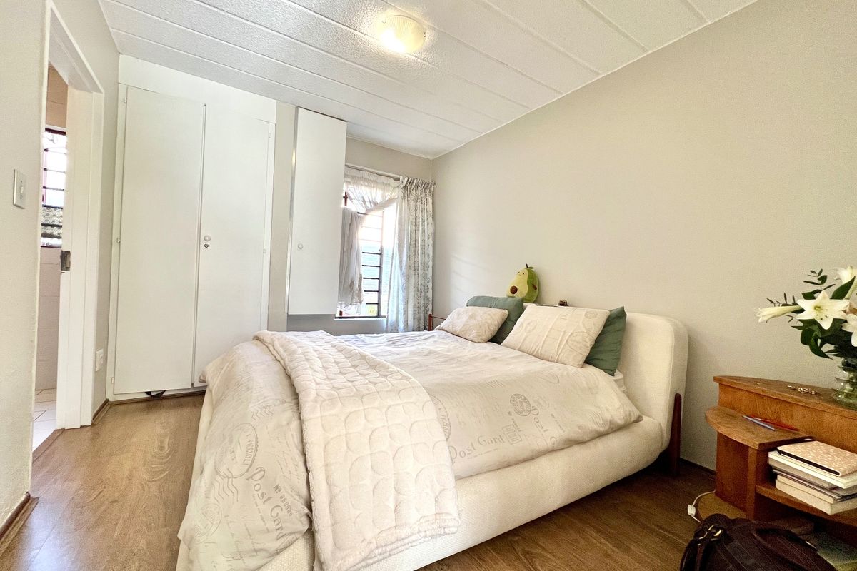 A functional bedroom featuring laminate flooring, built-in cupboards, and a window allowing natural light, providing a comfortable and practical living space.