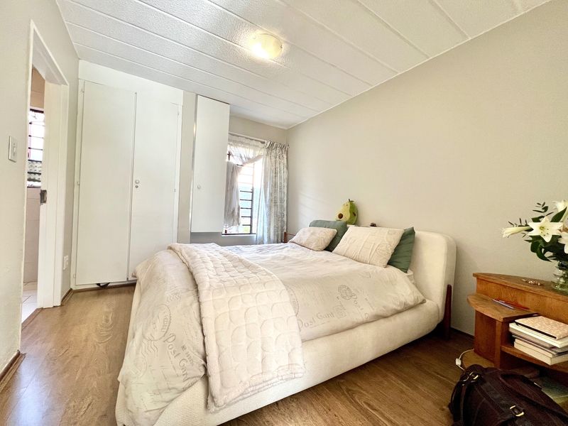 A functional bedroom featuring laminate flooring, built-in cupboards, and a window allowing natural light, providing a comfortable and practical living space.