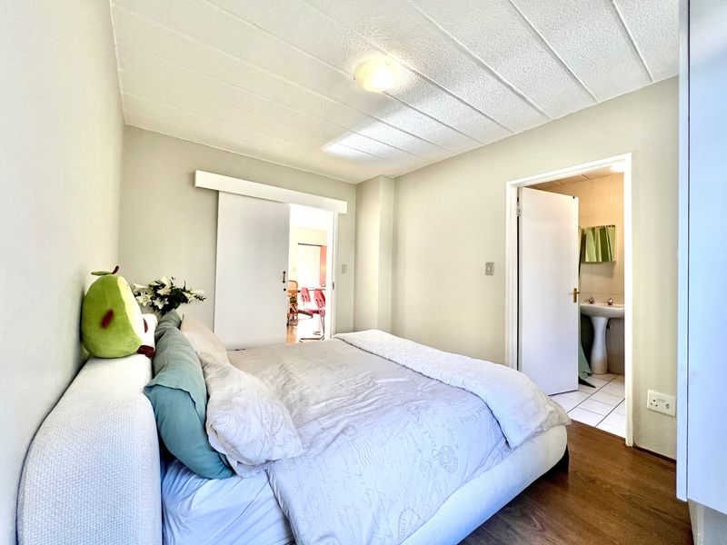 A bedroom featuring laminate flooring, a sliding door, and direct access to an en-suite bathroom with a pedestal basin.