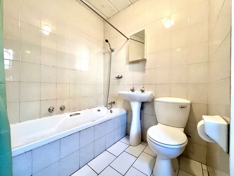 A dated bathroom featuring a pedestal basin, toilet, and bathtub with wall-to-wall tiling. The space is functional but requires cosmetic updates.