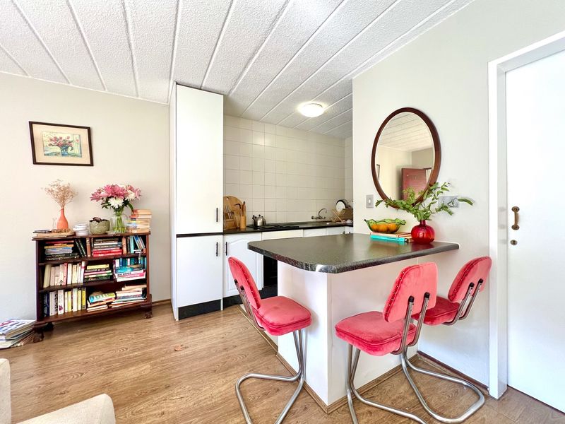 Open plan kitchen area featuring white cabinetry, a breakfast bar, tiled backsplash, and laminate flooring in a functional apartment layout.