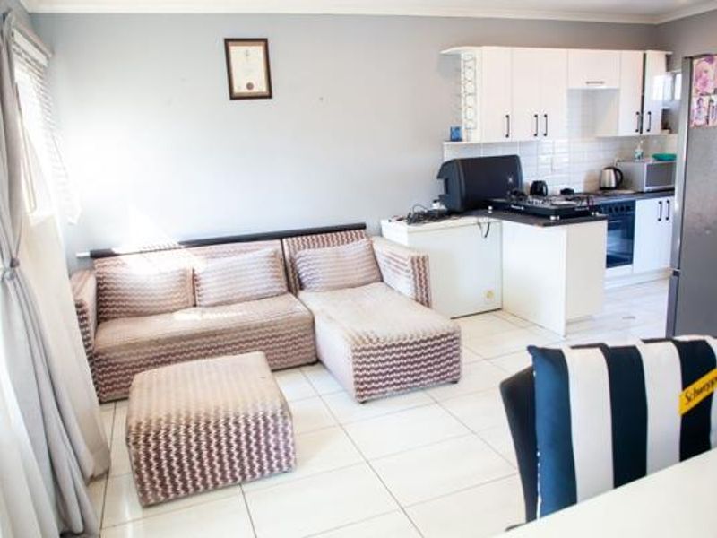 Open-plan living area featuring tiled flooring and a compact kitchen with built-in cabinetry, oven, and hob.