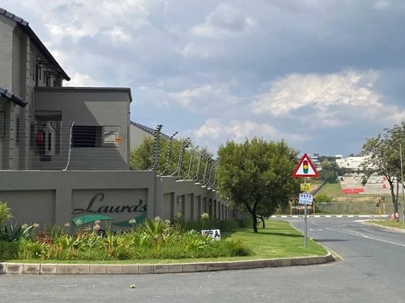 Street view of the apartment complex entrance featuring a boundary wall with electric fencing and landscaped verge.