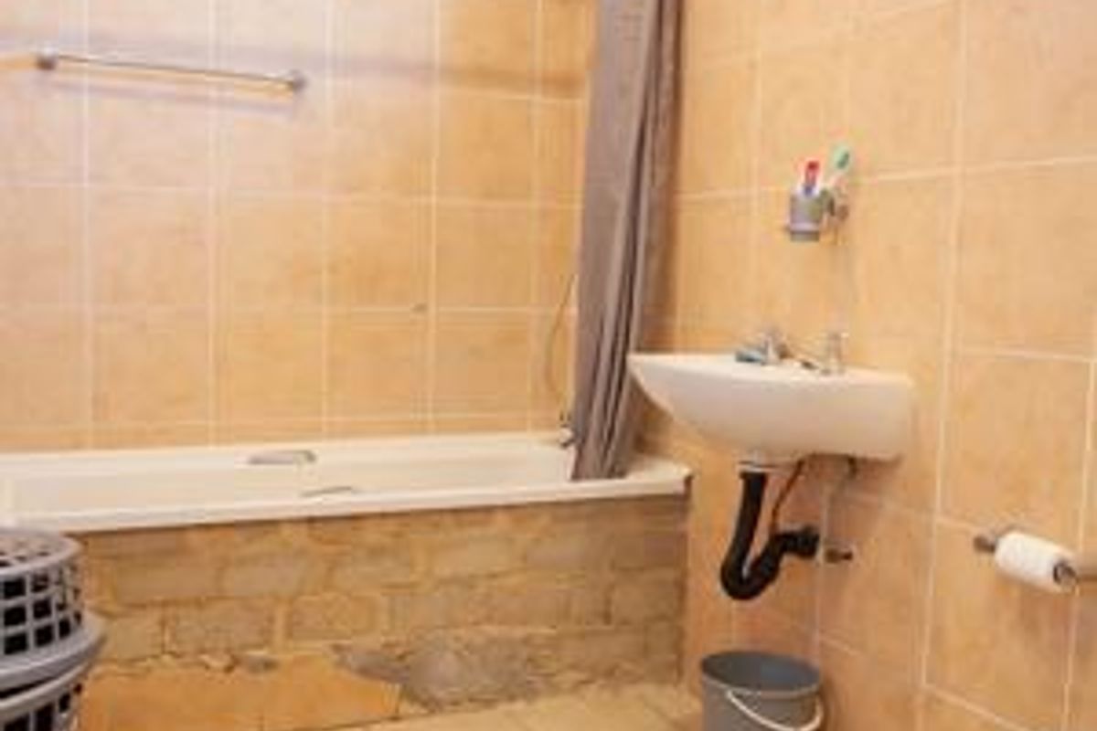 A functional bathroom featuring a bathtub, wall-mounted basin, and toilet, with tiled finishes. The bathtub apron requires repair and finishing.