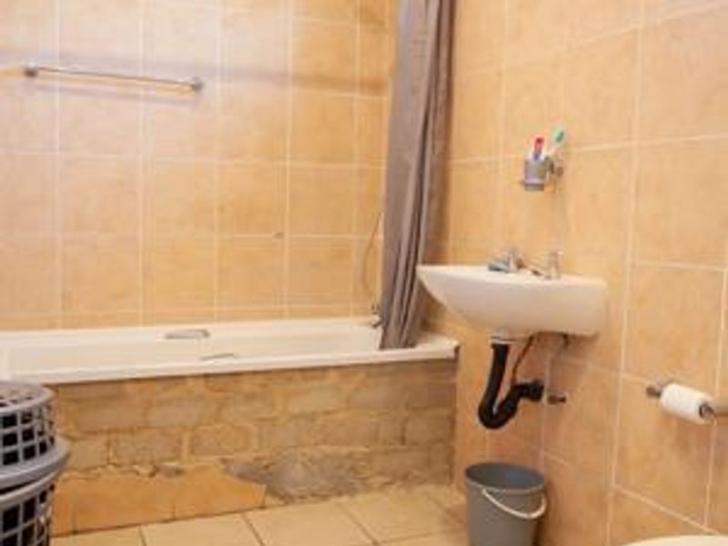 A functional bathroom featuring a bathtub, wall-mounted basin, and toilet, with tiled finishes. The bathtub apron requires repair and finishing.