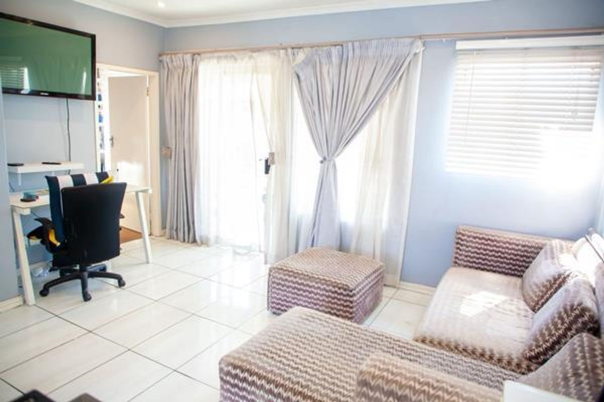 A bright living room featuring tiled flooring, large sliding glass doors with curtains, and venetian blinds, providing access to an outdoor area.