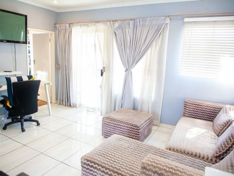 A bright living room featuring tiled flooring, large sliding glass doors with curtains, and venetian blinds, providing access to an outdoor area.