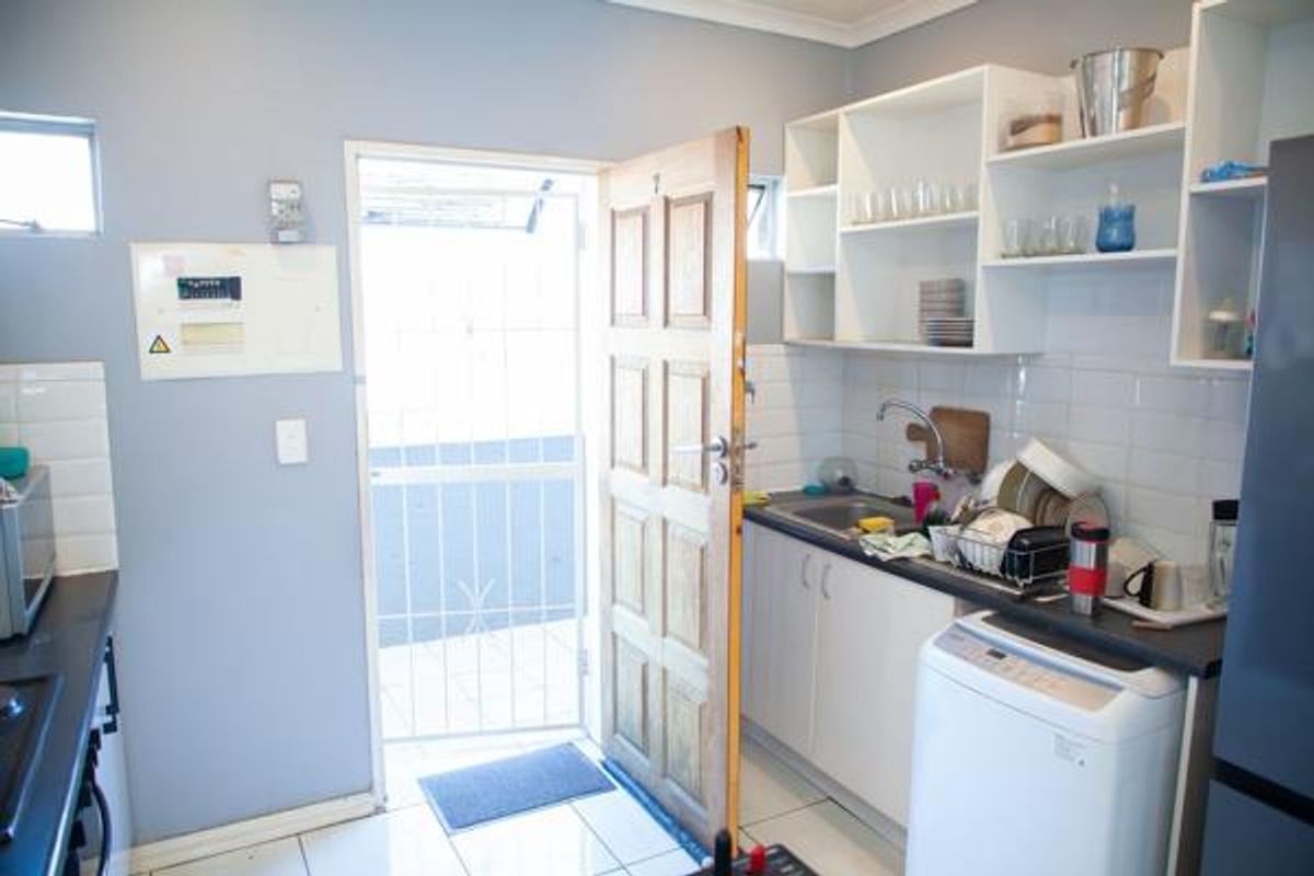 Functional scullery area featuring built-in cabinetry, stainless steel sink, tiled backsplash, and direct access to an exterior space via a security gate.